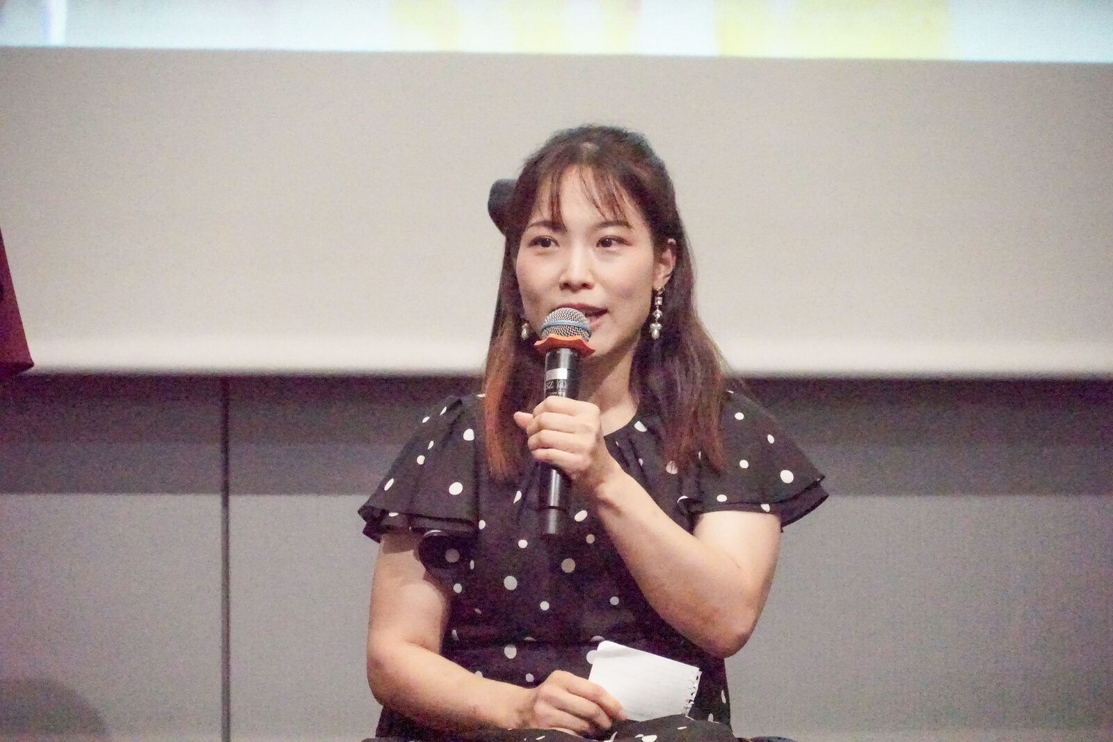 ドット柄のワンピースの愛澤咲月さんがマイクを持って話している。