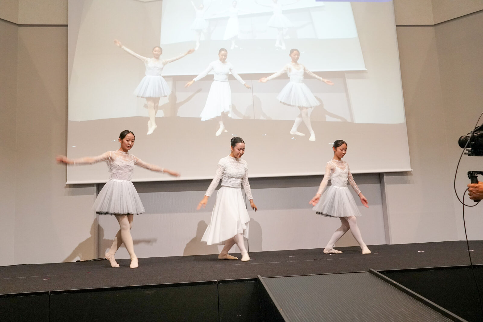 3人のバレリーナがランウェイ上で踊り、背面のスクリーンにその姿が大きく投影されている。