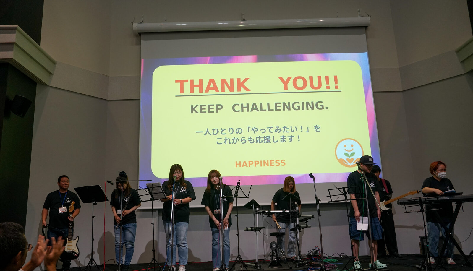 スクリーンに「THANK YOU!! KEEP CHALLENGING. 一人ひとりの『やってみたい!』をこれからも応援します!」と表示され、その前でバンドが演奏している。