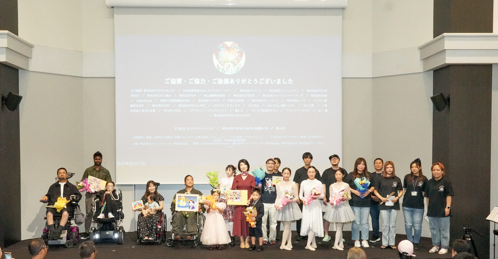 ステージ上に出演者とスタッフ全員が並んだ集合写真。花束を持つ人もいる。